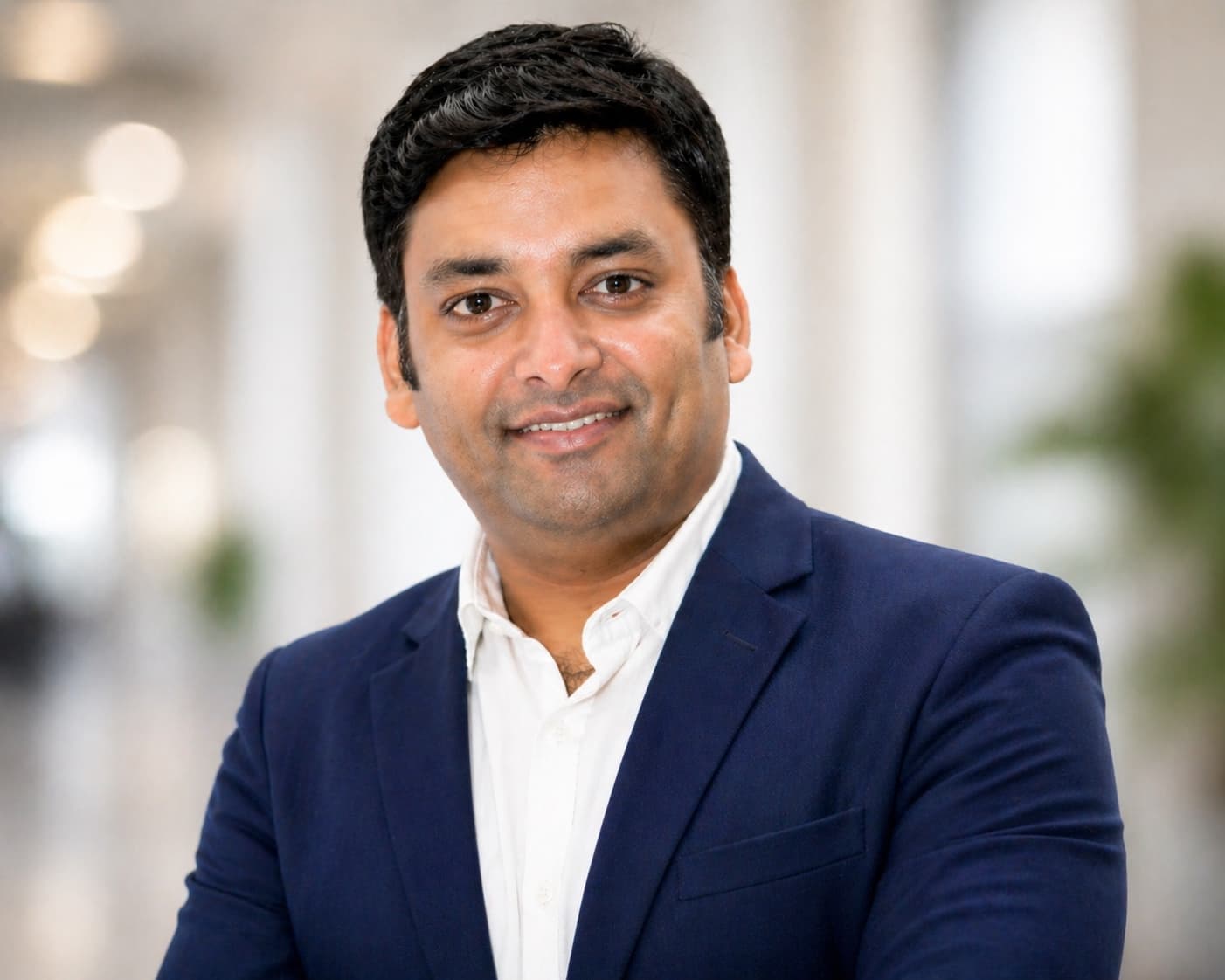 Chitiz Agarwal in a navy blazer and white shirt, smiling, in a bright office